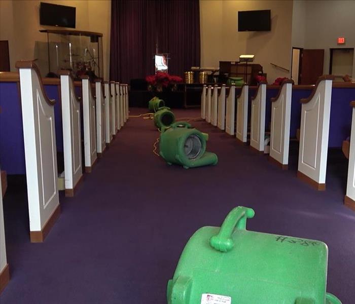 Air movers set up inside a church on carpeting with rows pews to either side